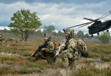 Mehrere Soldaten vom Fallschirmjägerregiment 31 hocken auf einer Wiese und sichern, im Hintergrund fliegt ein Hubschrauber weg.