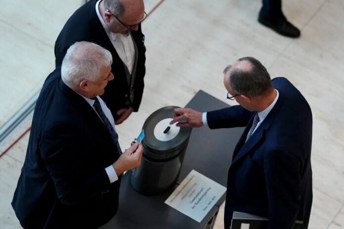Bundeskanzler Friedrich Merz (r.) gibt bei der namentlichen Abstimmung über das Gesetz für einen neuen Wehrdienst seine Stimmkarte im Bundestag ab.