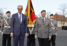 Bundeskanzler Friedrich Merz steht nach der Verleihung des Fahnenbands mit dem Kommandeur des Wachbataillons im BMVg vor der Truppenfahne.