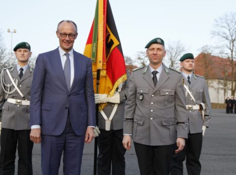 Bundeskanzler Friedrich Merz steht nach der Verleihung des Fahnenbands mit dem Kommandeur des Wachbataillons im BMVg vor der Truppenfahne.