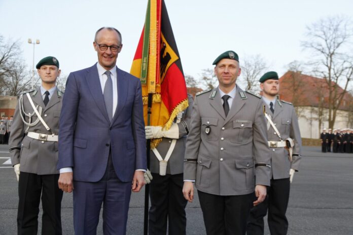 Bundeskanzler Friedrich Merz steht nach der Verleihung des Fahnenbands mit dem Kommandeur des Wachbataillons im BMVg vor der Truppenfahne.