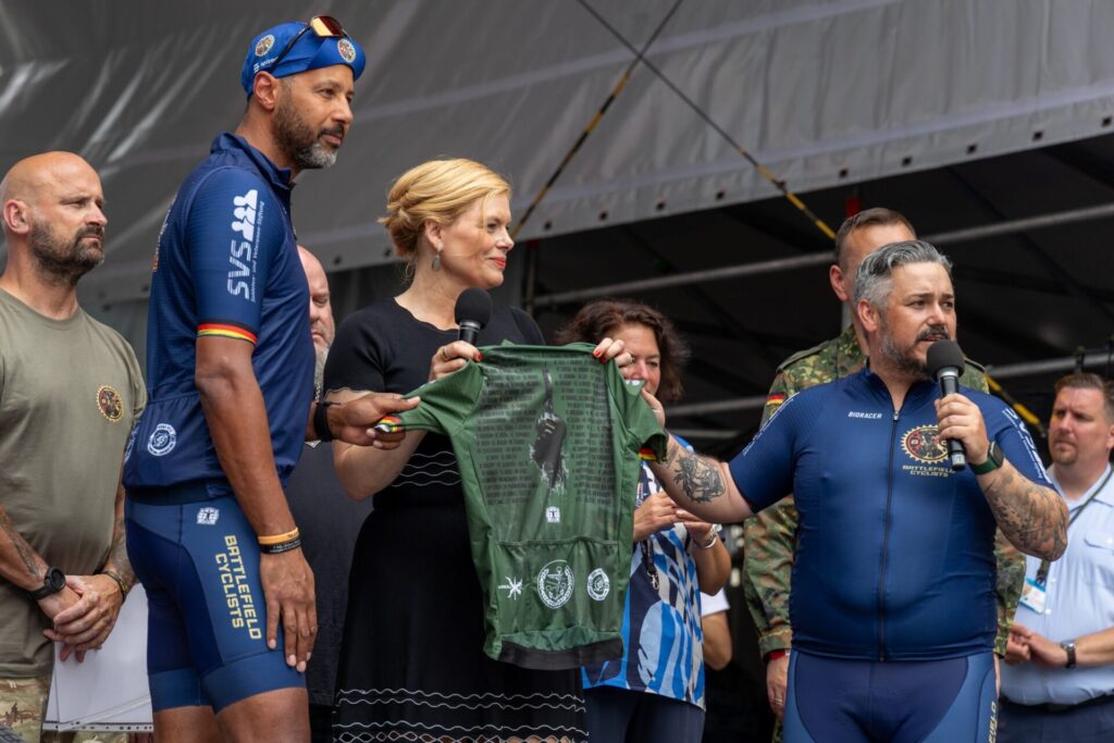 Veteranentag: Programm zur zentralen Festveranstaltung 2 Bundestagspräsidentin Julia Klöckner begrüßt am 15. Juni 2025 die “Battlefield Cyclists”, einen Zusammenschluss psychisch und physisch verwundeter Veteranen, auf der Bühne vor dem Deutschen Bundestag.